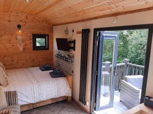 a bedroom with a bed and a balcony with a sliding glass door at Shepherds Hut with hot tub on Anglesey North Wales in Gwalchmai