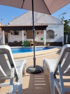 un par de sillas blancas y una sombrilla junto a una piscina en Casa Rural El Cornijal - Piscina Privada en San Javier