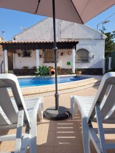 a pair of white chairs and an umbrella next to a pool at Casa Rural El Cornijal - Piscina Privada in San Javier