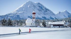 dos personas esquí de fondo frente a una iglesia y una montaña en Landgasthaus Birkegg, en Leutasch