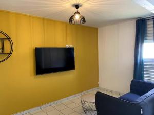 un salon avec une télévision sur un mur jaune dans l'établissement Appartement moderne, 2 chambres, proche aéroport • CHU • port, à Les Abymes