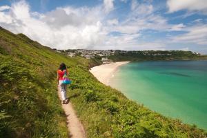 a woman walking down a path towards a beach at Menhyr in Carbis Bay