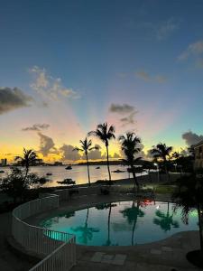 uma piscina com palmeiras e o oceano ao pôr do sol em Merveilleux studio cosy vue mer - piscine em São Martinho