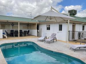 ein Swimmingpool mit Stühlen und einem Sonnenschirm auf einer Terrasse in der Unterkunft Coghill House in Yarrawonga