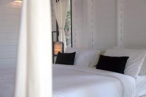 a white bed with black pillows in a room at Barefoot Project formerly Baan Klong Kleng in Ko Phayam