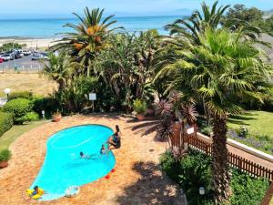einen Blick über einen Pool mit Palmen und den Strand in der Unterkunft Apartment18Lifestyle Gordons Bay Beachfront in Gordonʼs Bay