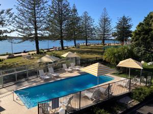 uma piscina com guarda-sóis e cadeiras e a água em The Mid Pacific em Port Macquarie