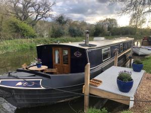 a boat tied to a dock with a table and plants at Willow - Cottage on the River, Luxury Houseboat in Little Baddow