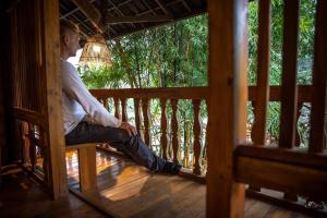 un hombre sentado en un banco de madera en un porche en Sapa Riverside Ecolodge & Spa, en Sa Pa