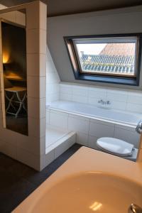 een badkamer met een bad, een toilet en een raam bij Yep! Slapen bij de Sluis in Blokzijl