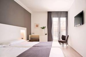 a bedroom with a bed and a chair and a television at Mar Calma Hotel in Port de Pollensa