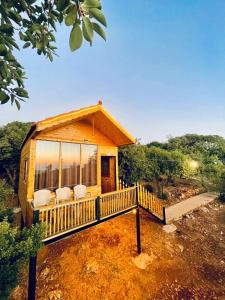 Cabaña de madera con porche y 2 sillas blancas en Ajloun Wooden Huts اكواخ عجلون الخشبية Live amid nature, en Umm al Manābī‘