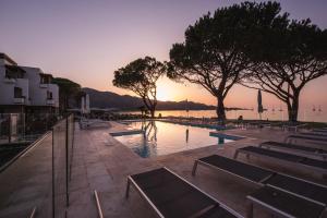 a swimming pool with a sunset in the background at Hôtel La Roya in Saint-Florent