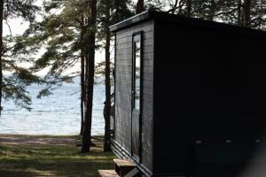 a black building with a bench in front of the water at Beach Cottage in Hanko
