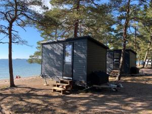 ein schwarzes winziges Haus am Strand mit Bäumen in der Unterkunft Beach Cottage in Hanko