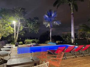 a pool with chairs and palm trees at night at Villa Jujubes in Le Bois de Nèfles
