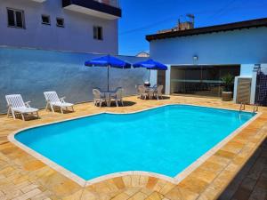 een groot blauw zwembad met stoelen en parasols bij 100mts DA PRAIA com Churrasqueira, Piscina e Wi-Fi in Caraguatatuba