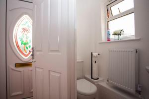 a white bathroom with a toilet and a window at Cozy 3-Bedroom Home in Luton in Luton