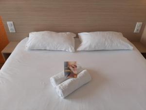 Una cama blanca con dos almohadas y una revista. en Première Classe Mâcon Sud en Chaintré