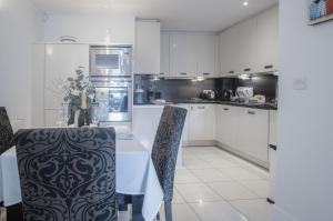 Minarvon - 2 Bedroom Apartment - Saundersfoot في ساندرزفوت: مطبخ مع دواليب بيضاء وطاولة وكراسي