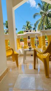 uma varanda com cadeiras amarelas, uma mesa e palmeiras em Villa Marcia em Boca Chica
