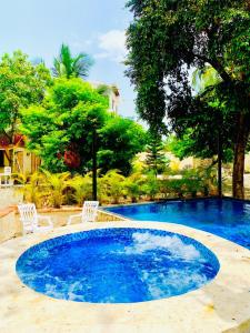 a large blue pool with two white chairs and trees at Villa Marcia in Boca Chica