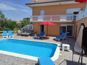 a pool with chairs and an umbrella and a house at Apartment Danica in Poličnik