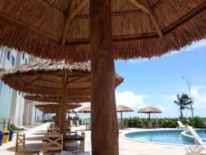 a resort with a pool and straw umbrellas and chairs at Apartamento com 2 quartos de FRENTE PARA O MAR in Maceió