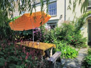 einen Holztisch mit einem orangenen Regenschirm im Garten in der Unterkunft The Shire House in Lostwithiel