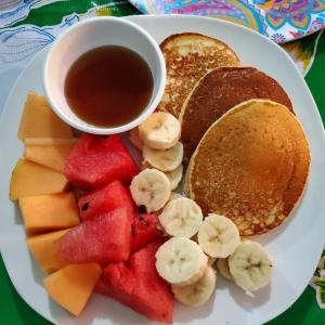 a plate of pancakes and fruit and a cup of syrup at Sunset Bay House in Six Huts