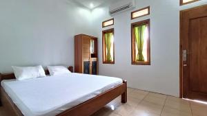1 Schlafzimmer mit einem weißen Bett und 2 Fenstern in der Unterkunft Jogo Segoro Homestay Mitra RedDoorz near Pantai Sundak Gunungkidul in Ngandong