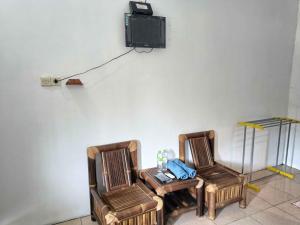 2 Stühle und ein Tisch mit einem TV an der Wand in der Unterkunft Jogo Segoro Homestay Mitra RedDoorz near Pantai Sundak Gunungkidul in Ngandong