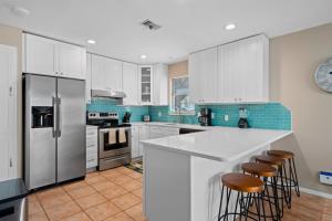 cocina con armarios blancos, nevera y taburetes en Gone Coastal, en Rockport