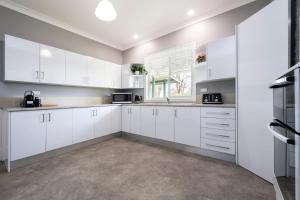 a kitchen with white cabinets and a window at Tatbern Park Cottage Wallalong in Wallalong