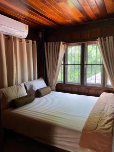 a bedroom with a large bed with two windows at Traditional Thai house บ้านเรือนไทย ใกล้หาดระยอง in Ban Chak Phai