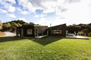 a black house on a green lawn at Modern Raglan Hideaway in Raglan