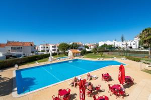 a large swimming pool with red chairs and people sitting around it at SILCHORO - Estúdio remodelado com AC e piscina em Albufeira in Albufeira