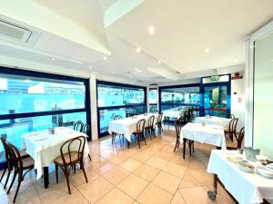 un restaurante con mesas y sillas blancas y ventanas en Hotel Venere en Cesenatico