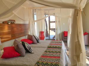 a bedroom with a canopy bed with red pillows at Okutala Etosha Lodge in Outjo