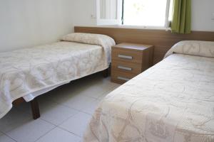 a bedroom with two beds and a dresser and a window at Apartamentos Playa Calan Blanes in Cala en Blanes