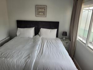 a bed with white sheets and pillows next to a window at RentUnique Central Caledonian house cosy home in Crawley