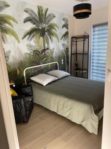 1 dormitorio con 1 cama con palmeras en la pared en Studio cosy avec en option piscine accessible de avril à octobre, en Quimperlé