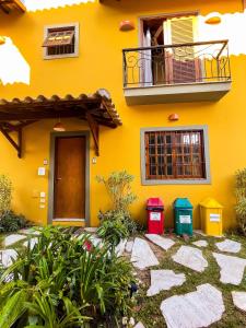 une maison jaune avec un balcon et deux poubelles dans l'établissement Recanto das Tiribas, à Ilhabela