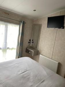 a bedroom with a bed and a television on the wall at Sunrise - Beautiful lakeside caravan in South Cerney