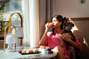 a woman sitting in a chair with a dog eating food at Kimpton Aysla Mallorca by IHG in Santa Ponsa