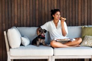 a woman sitting on a couch eating food with a dog at Kimpton Aysla Mallorca by IHG in Santa Ponsa