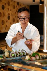 a man in a kitchen preparing food with a spoon at Kimpton Aysla Mallorca by IHG in Santa Ponsa