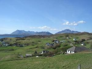 a green field with houses and mountains in the background at Braeside cottage in Tarskavaig