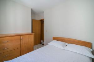 1 dormitorio con cama blanca y tocador de madera en Aluguel Apartamento 2 quartos 100m Mar Bombas/SC, en Bombinhas