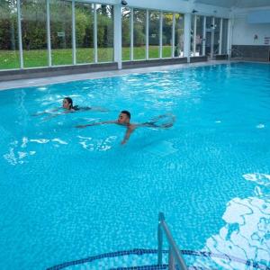 two people swimming in a large swimming pool at Macdonald Craxton Wood Hotel & Spa in Ledsham